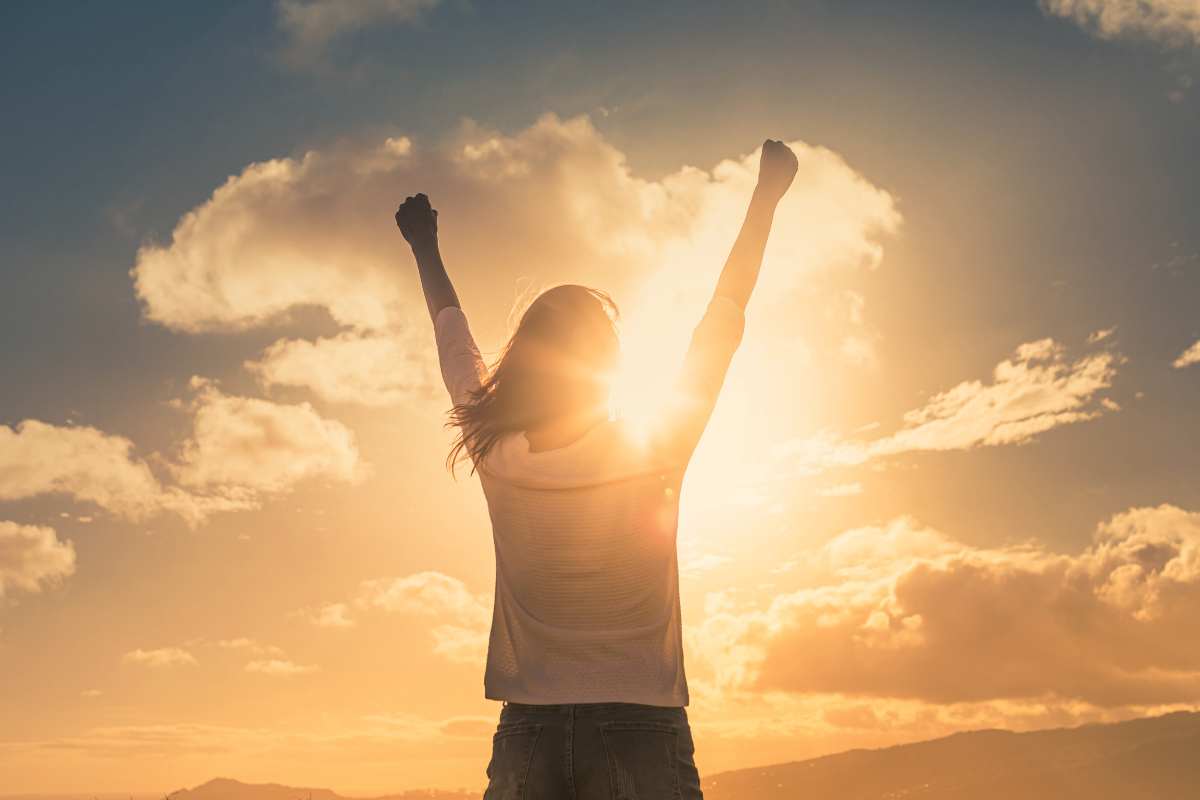 kobieta unosi rece w gorze w geście triumfu na tle nieba podczas zachodu slonca
